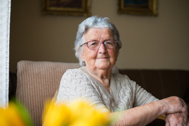 Portrait of a beautiful old woman with gray hair and glasses is sitting in a chair in her home.