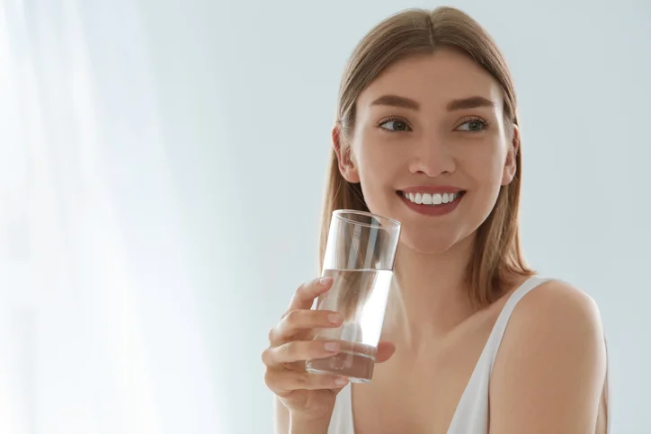 Woman with glass of fresh water in white portrait Woman with glass of fresh water in white portrait. Beautiful smiling girl with healthy skin and beauty face holding pure mineral water in glass indoors