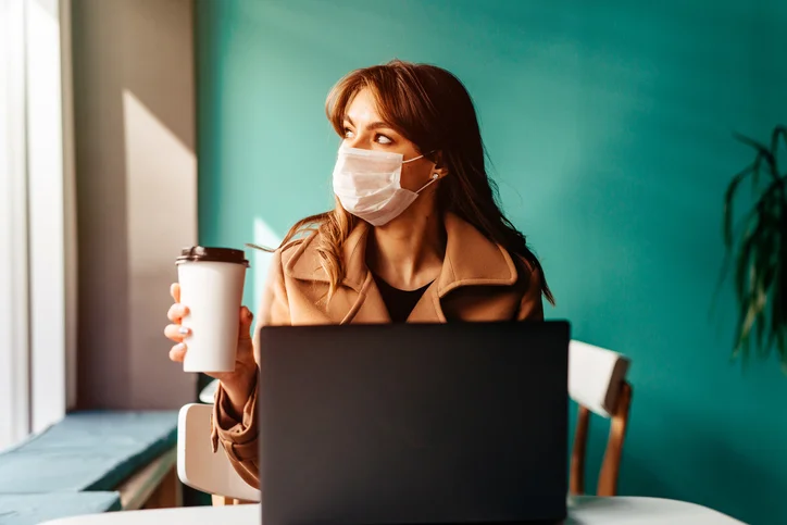 Woman in a protective mask sits in a cafe at a laptop. Protecting the population from coronaviruses by protecting the respiratory tract